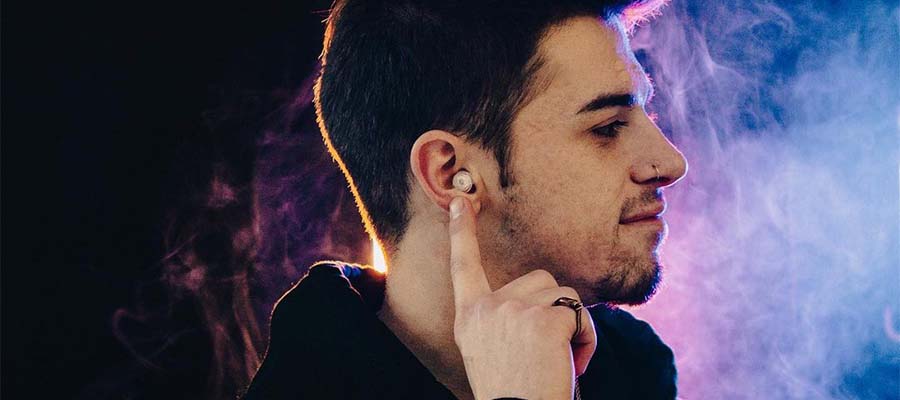 Man on the dark background is pointing at the earplug in his ear