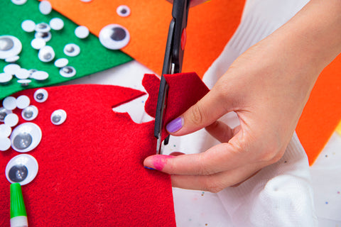 cutting lip shape out of red felt for sock puppet with supplies in background