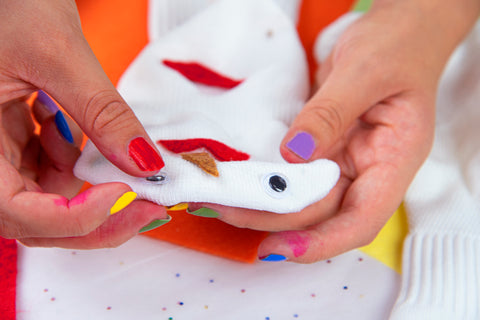 applying googly eye to sock puppet with colorful nails and speckled background