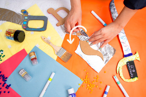 wrapping cardboard sword in tinfoil on colorful background with craft supplies and finished craft swords