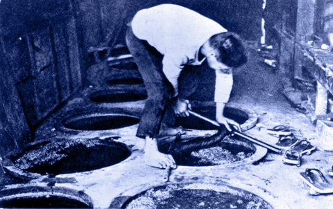 indigo hued black and white image of a man dyeing fabric in indigo dye pits in Okinawa before 1946