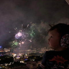 um bebê usando proteção auditiva infantil banz assiste fogos de artifício no céu noturno