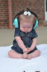 Young child in baby earmuffs in denim outfit looking at own toes