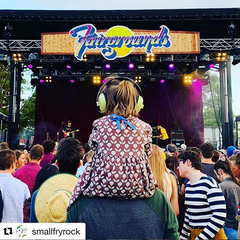 Young child at concert outdoor facing stage on adult shouldwers wearing banz earmuffs