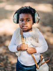 Young child in baby earmuffs, wearing a vestr and purse in outdoor setting