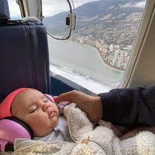 Un bebé duerme en un avión con orejeras Banz y vistas desde la ventanilla del avión en la costa.