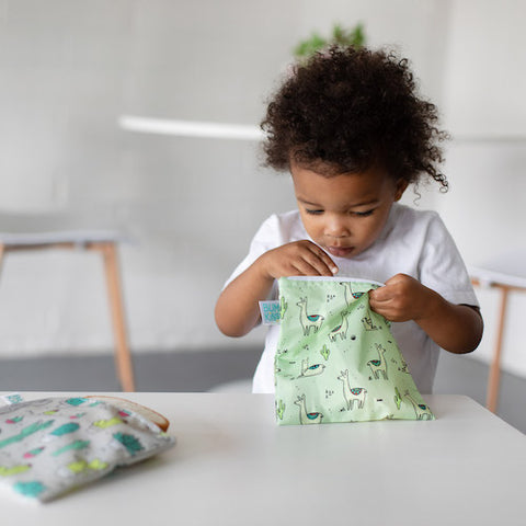 toddler looking in a reusable sandwich bag with llamas on it