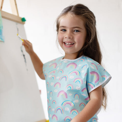 young girl painting in a rainbow art smock