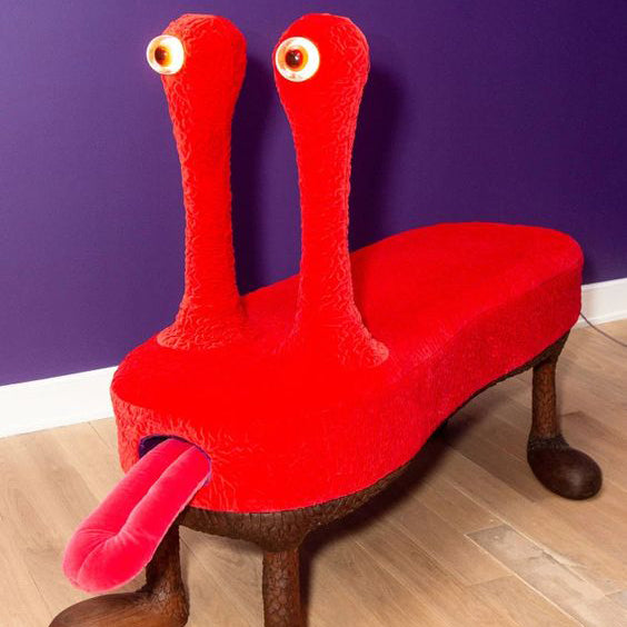 a bright red alien-anthromorphic bench in front of a purple wall