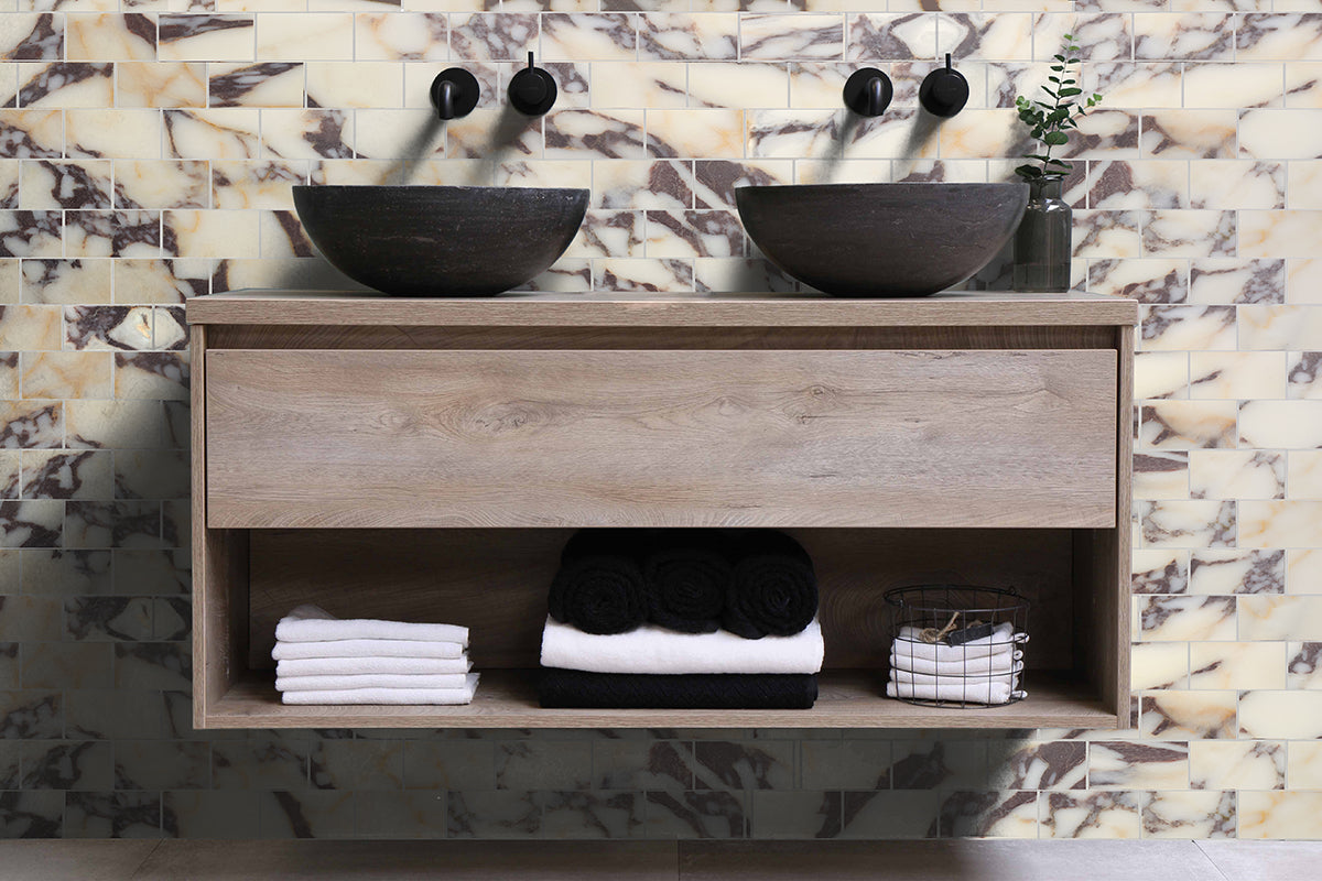 Bathroom double sink area with calacatta viola marble tile wall, floating wood cabinet, and black sinks.