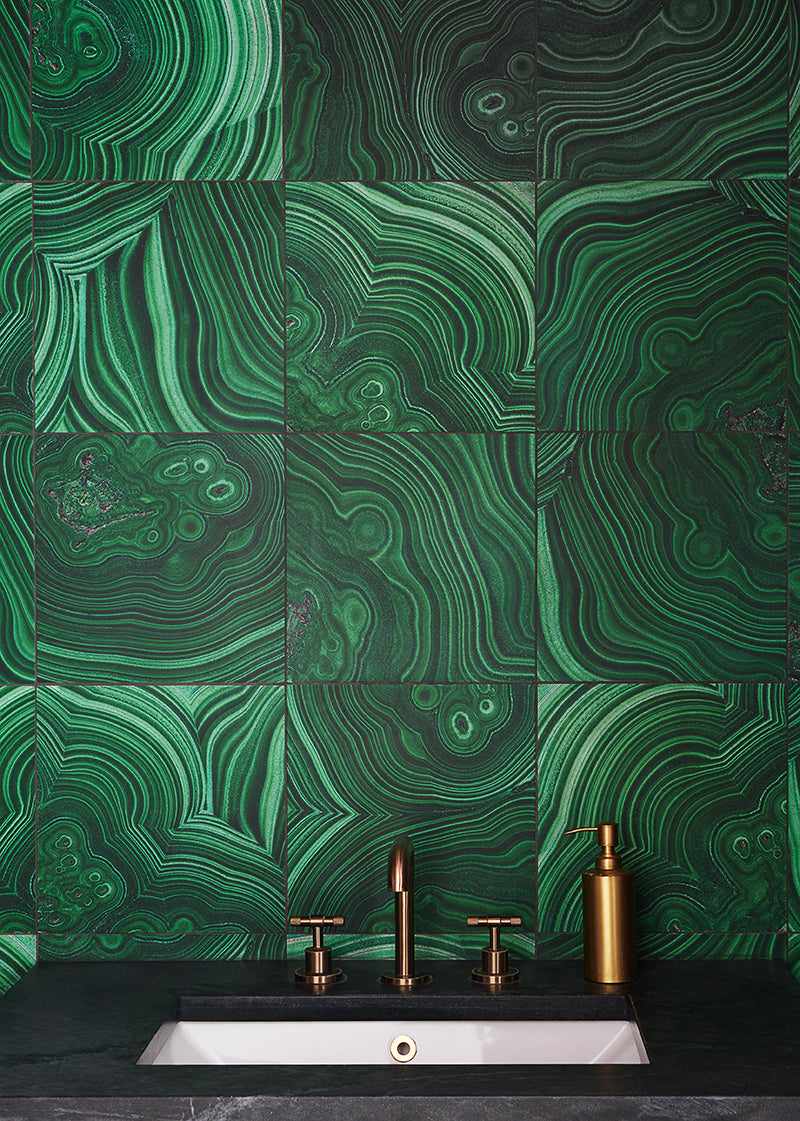 Bright bathroom sink area with a green swirl tile backsplash, black counter, and brass hardware.