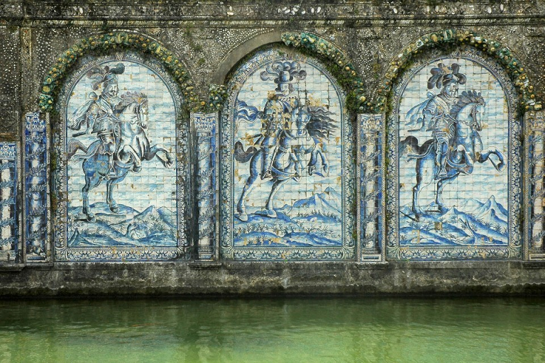 Three azulejos installations on a wall under arches depict three knights on horseback with fancy hats.