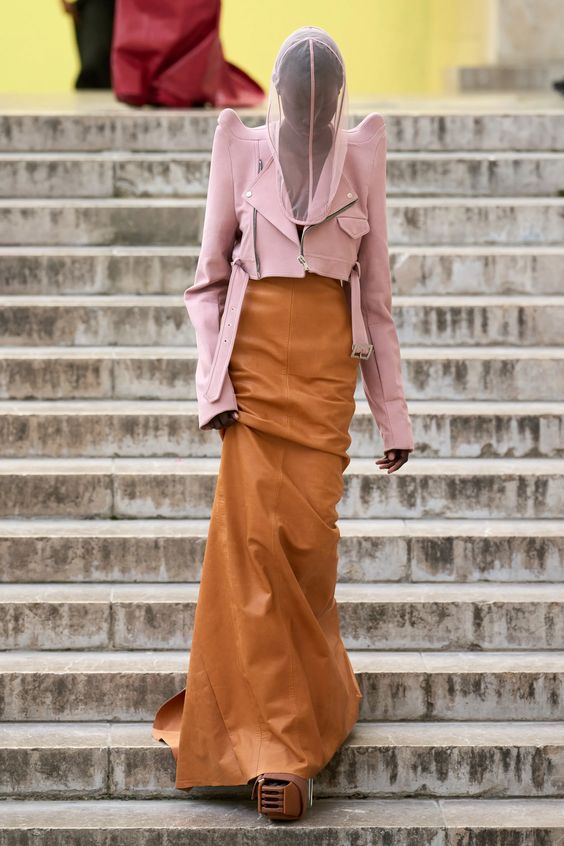 woman walking on runway wearing a pink blazer and orange skirt 