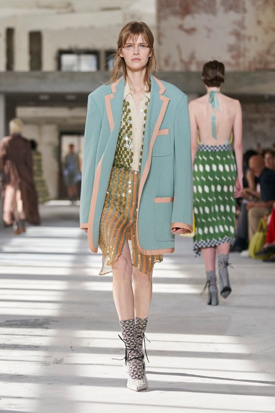 woman walking runway wearing blue blazer and sequin skirt