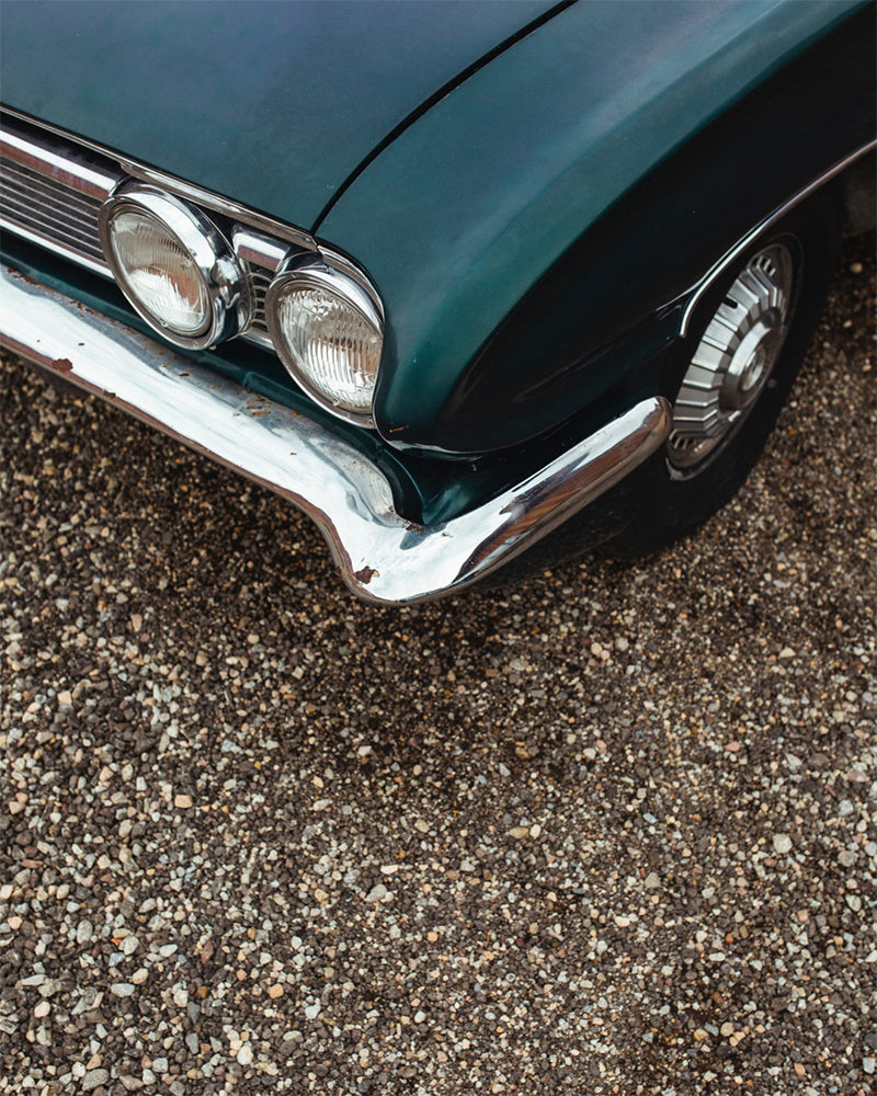 A dark turquoise vintage car and gravel.