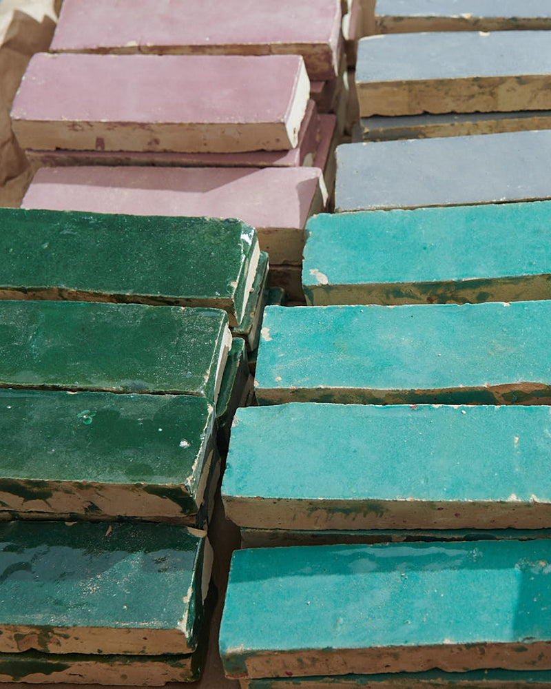 Stacks of colorful glazed zellige tile in green, turquoise, pink, and grey.