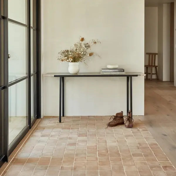 Open entryway with narrow black-legged table and a natural zellige tile floor.