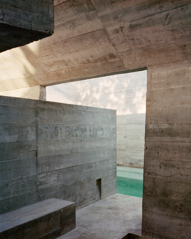 Board-formed concrete walls, bench and a glimpse of turquoise pool.