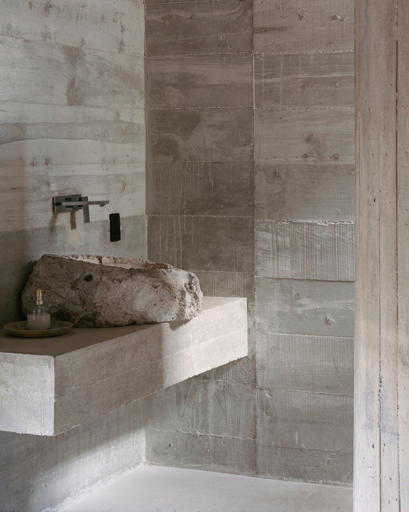 Board-formed concrete walls and a thick cantilevered concrete sink with an unfinished piece of stone used as a basin.