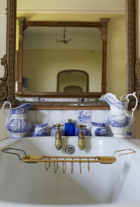Delft tiles and blue and white pitchers above a bathtub.