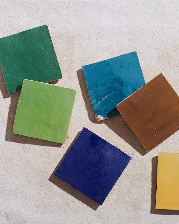Stylistic overhead shot of square zellige tiles in green, blue, brown, and yellow.