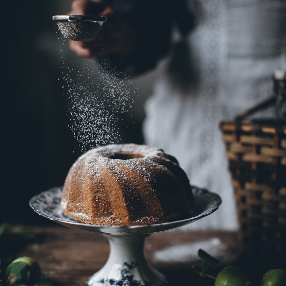 a chef shakes sugar over a bundt cake
