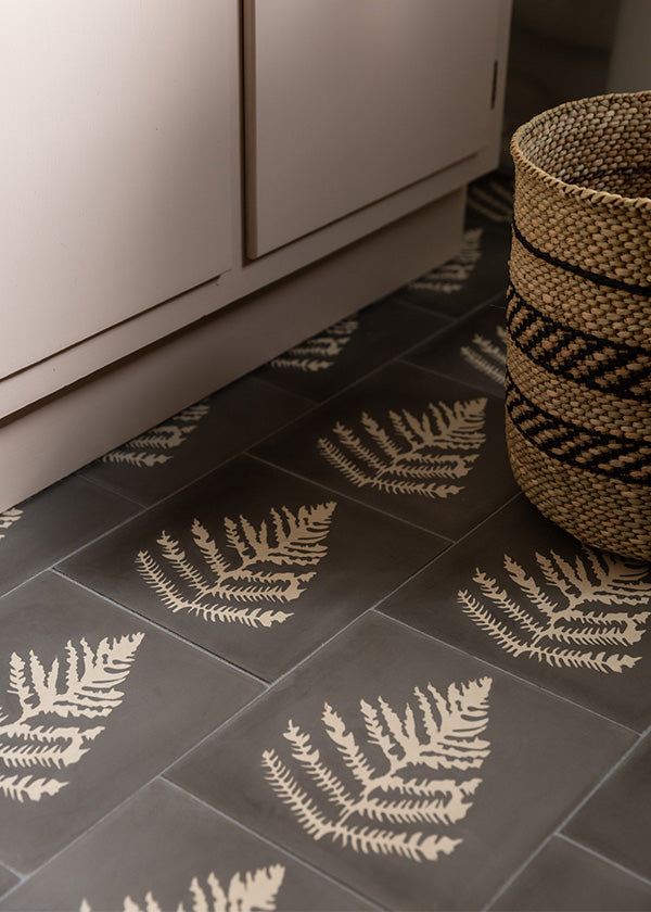 Closeup of matte black cement tile floor with a light colored fern on each tile.