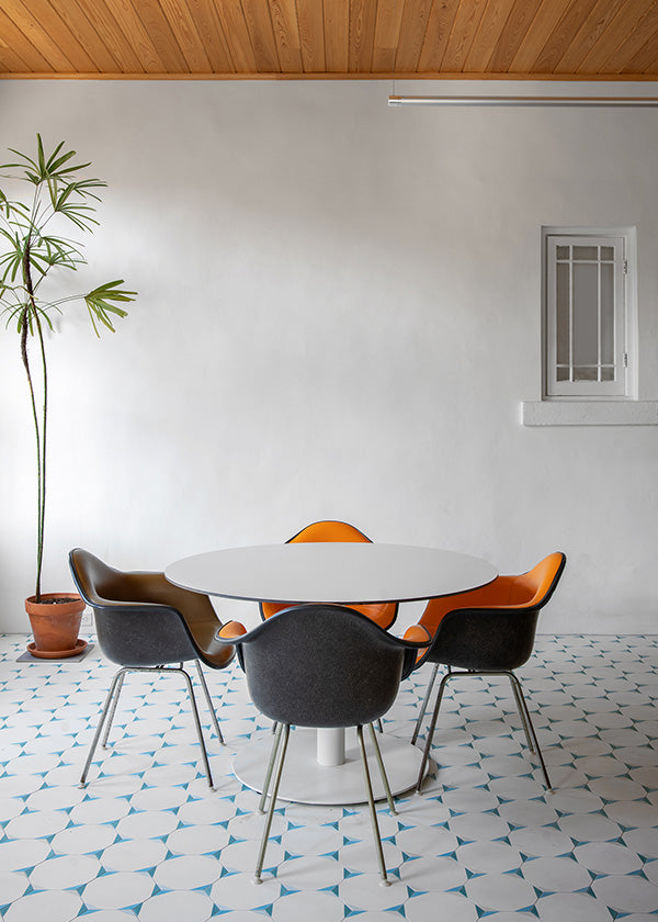 Bright and open seating area with a white and green cement tile floor, white walls, a white table, and orange chairs.