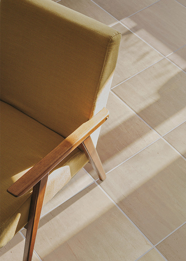 Artistic shot of the edge of a mid-century yellow chair casting a shadow on a limestone tile floor.