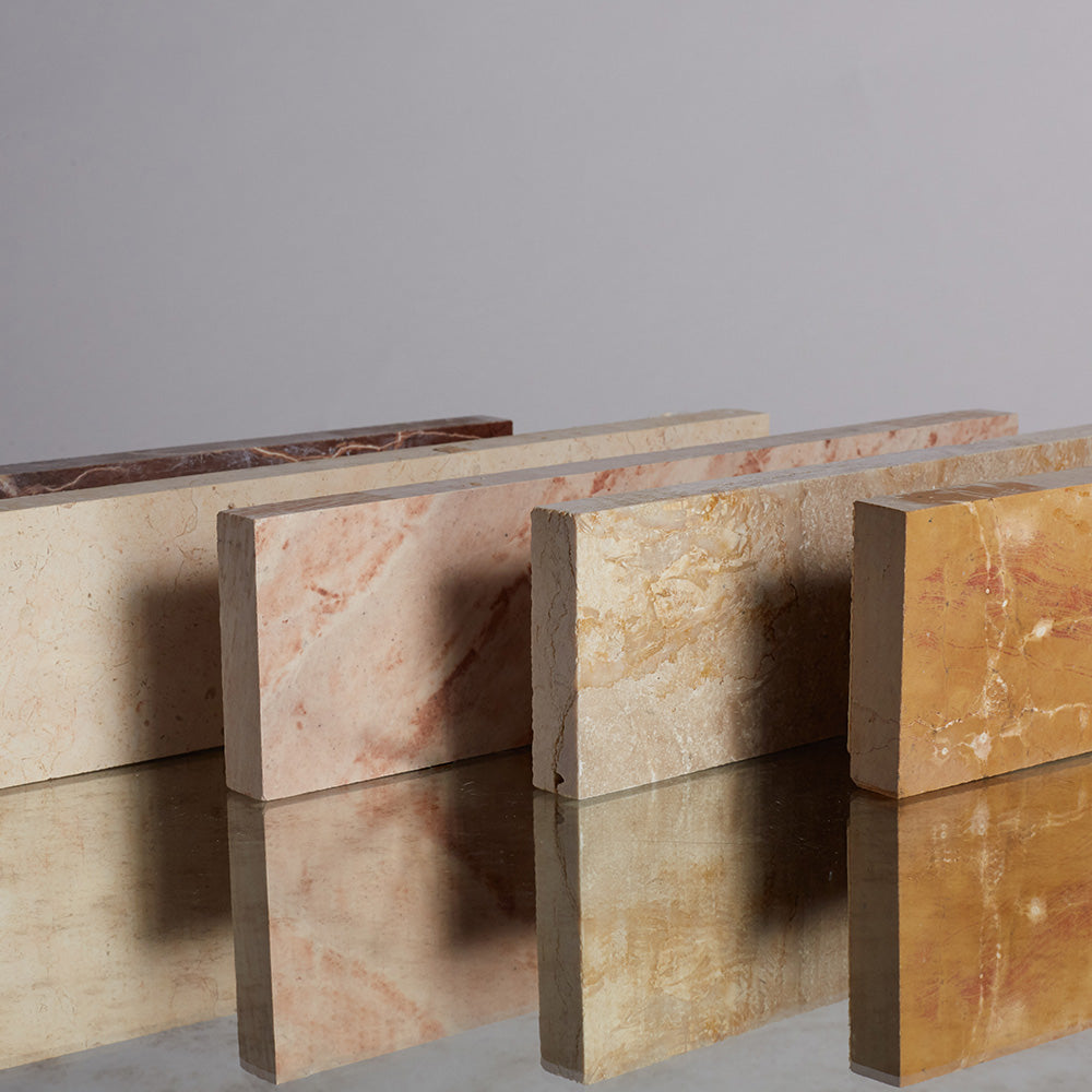 Stylistic array of clé strata linea natural stone tiles, standing upright in colors from light tan to dark pink and yellow.