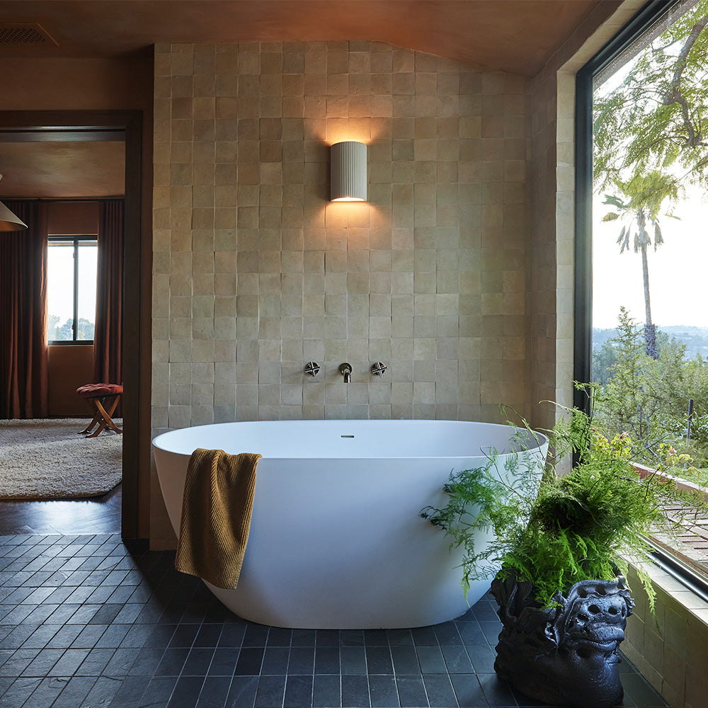 Wabi sabi style bathroom with natural zellige wall tile, slate floor tile, and a large white soaking bath tub.