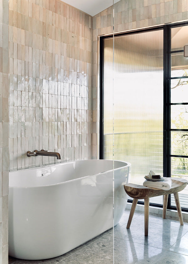 Sunlit wabi sabi style soaking bath tub area with cream colored eastern elements terracotta wall tile.