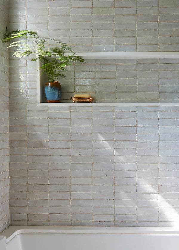 Off-white shower area with glazed zellige tile wall, a recessed tiled shelf, and a plant sitting inside.
