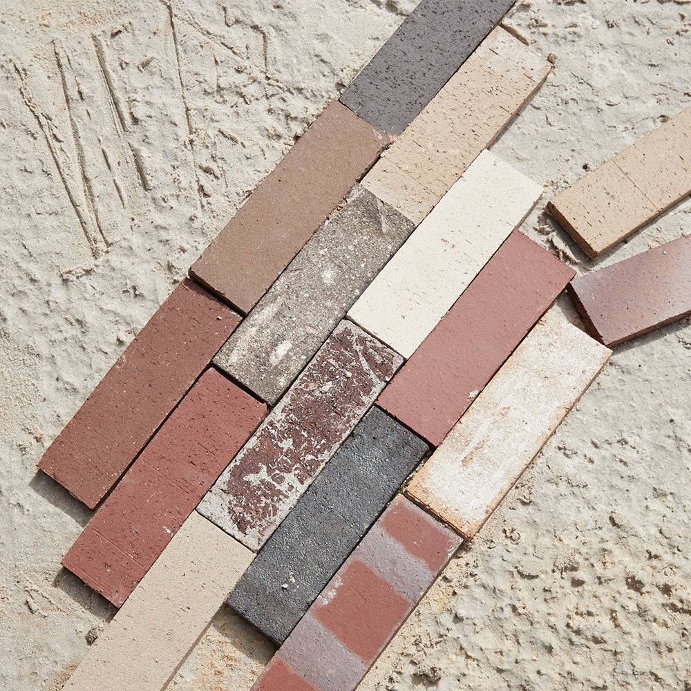 Assorted of patinated terracotta tiles stacked against a sandy background.