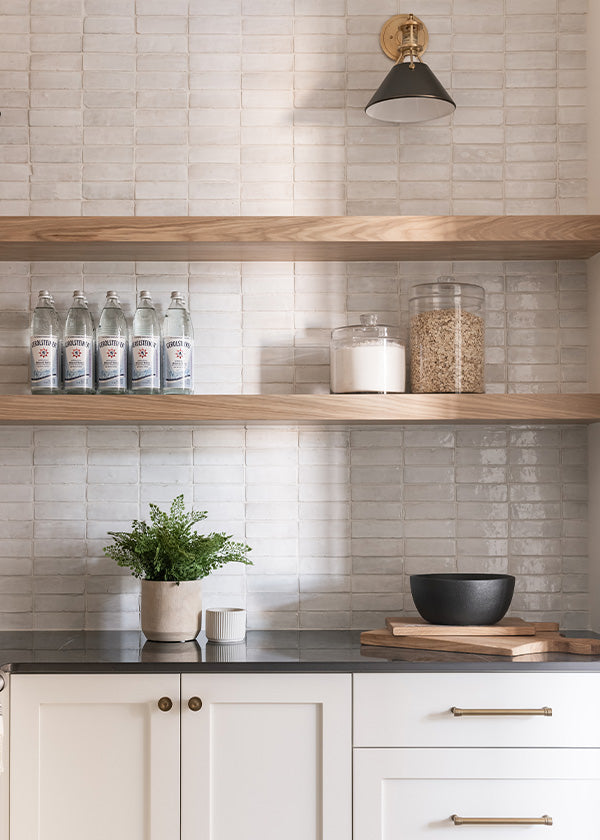 Light kitchen area with an off-white zellige tile wall, wood open shelves, and white lower cabinets.