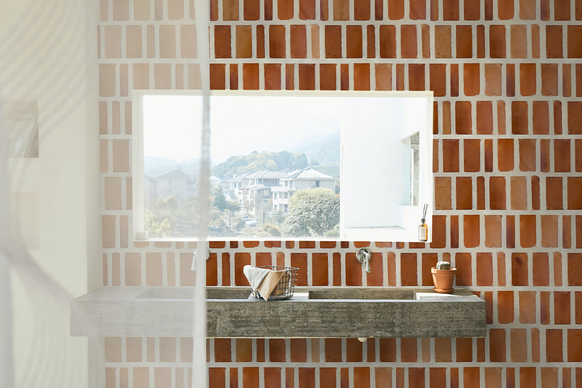 Airy bathroom with red terracotta tile wall featuring varied size tile.