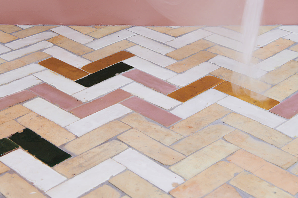 Closeup of multicolored zellige tile floor in herringbone pattern with pink wall.