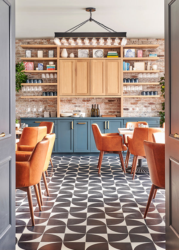 French inspired dining area with blue and oak cabinets, a brick wall, and a windmill cement tile floor.