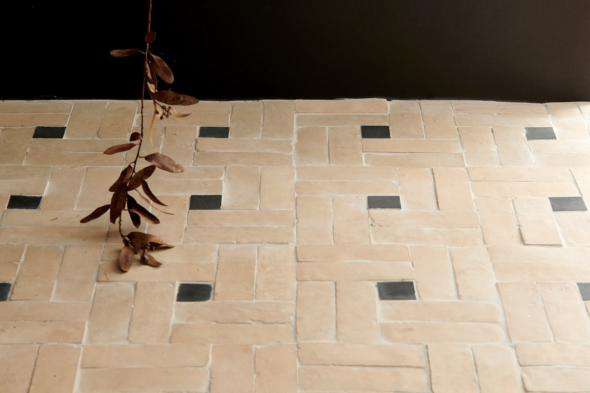 Light tan unglazed zellige tile floor laid in pinwheel pattern around small black square tiles.