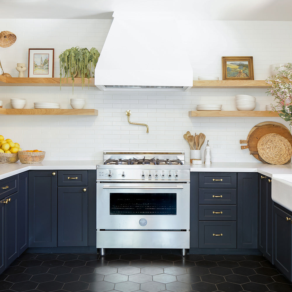 Modern kitchen with white subway tile walls, black cement floors, black cabinets, open shelving, and gold accents.