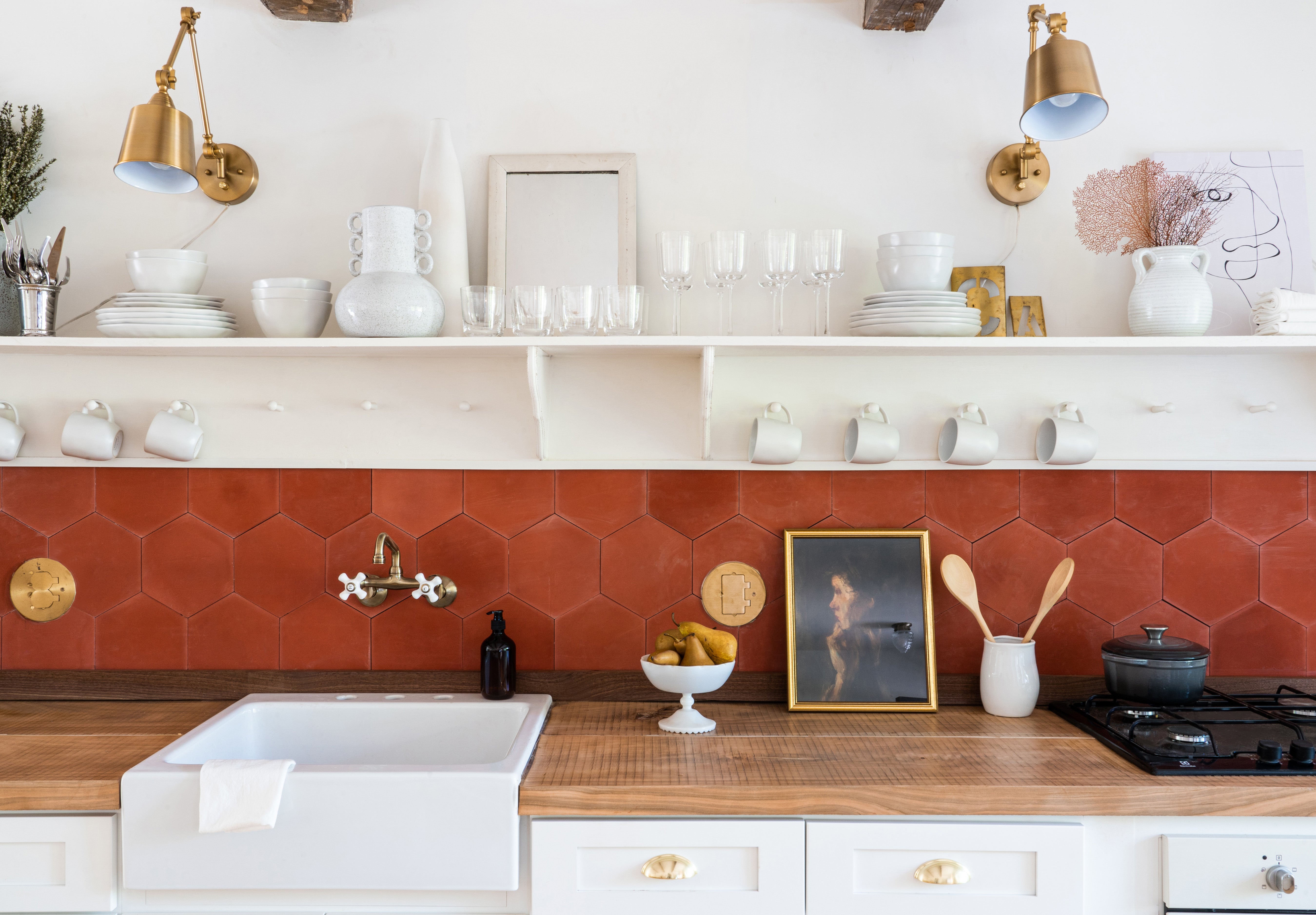 Bright kitchen sink area with a brick red hexagon cement tile backsplash, white walls, and butcher block countertops.