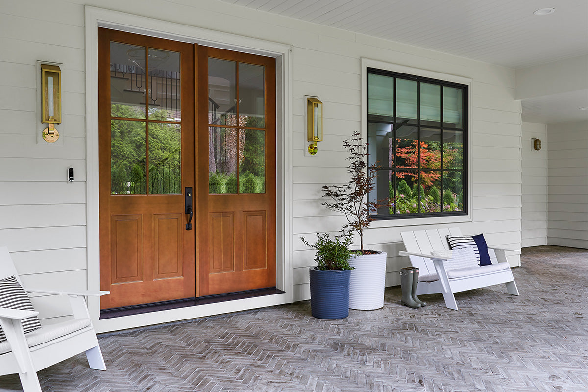 A beautiful white house's covered porch area with a floor of grey terracotta tile laid in a herringbone pattern.