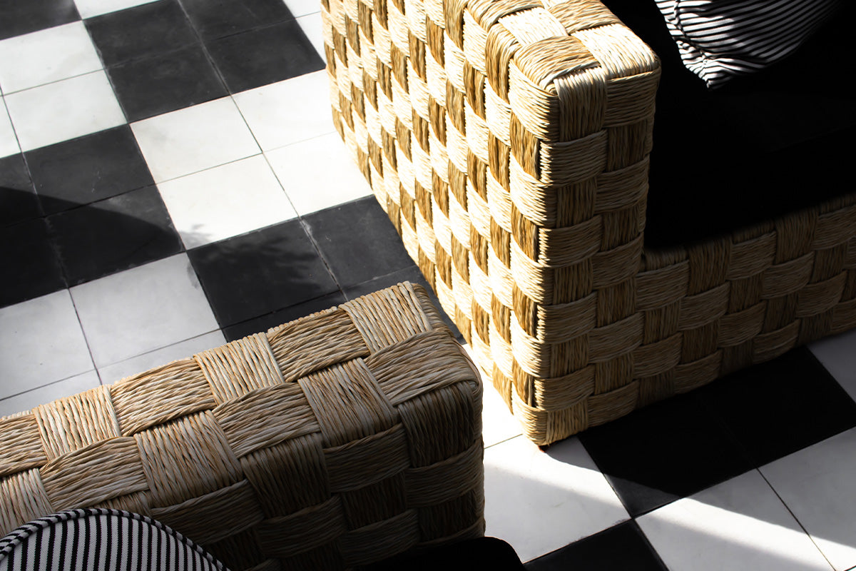Sylized shadowy photo of a black and white checkered tile floor with natural woven outdoor furniture.