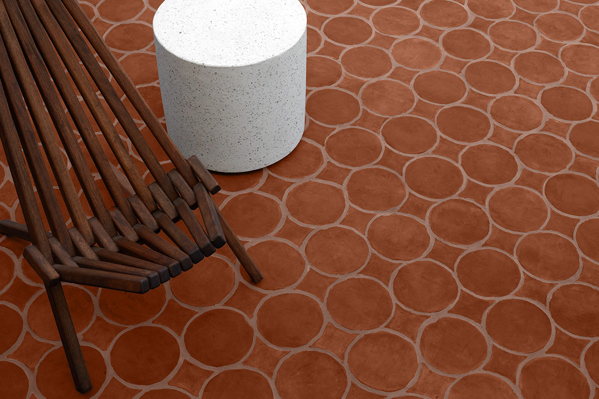 Closeup of red circle terracotta tile floor in an outdoor area with a wooden bench and marble side table.