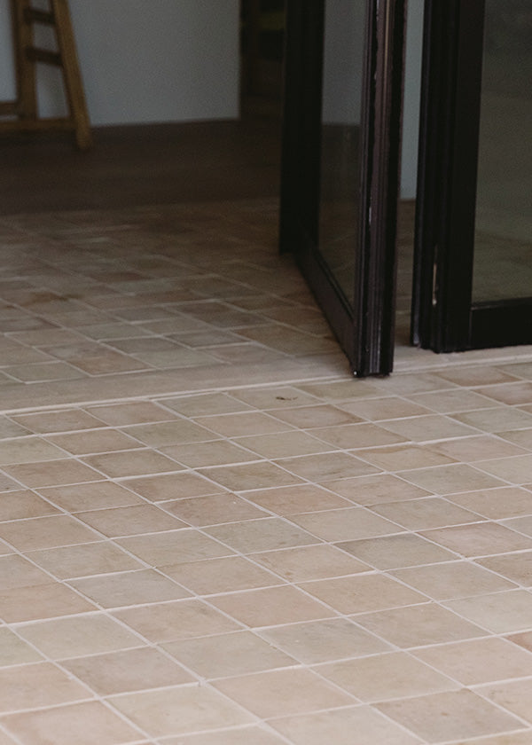 Closeup of an unglazed square zeillge tile floor that leads from an indoor space to an outdoor space.