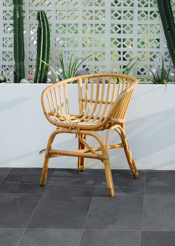 Rattan chair sitting in an open Southwest-inspired outdoor space with dark grey slate tile flooring and white walls.