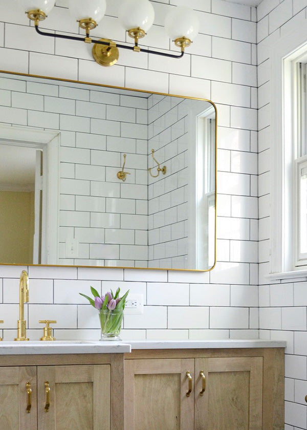 Bright and classic bathroom vanity area with glossy white subway tile wall, wooden cabinets, and gold accents.