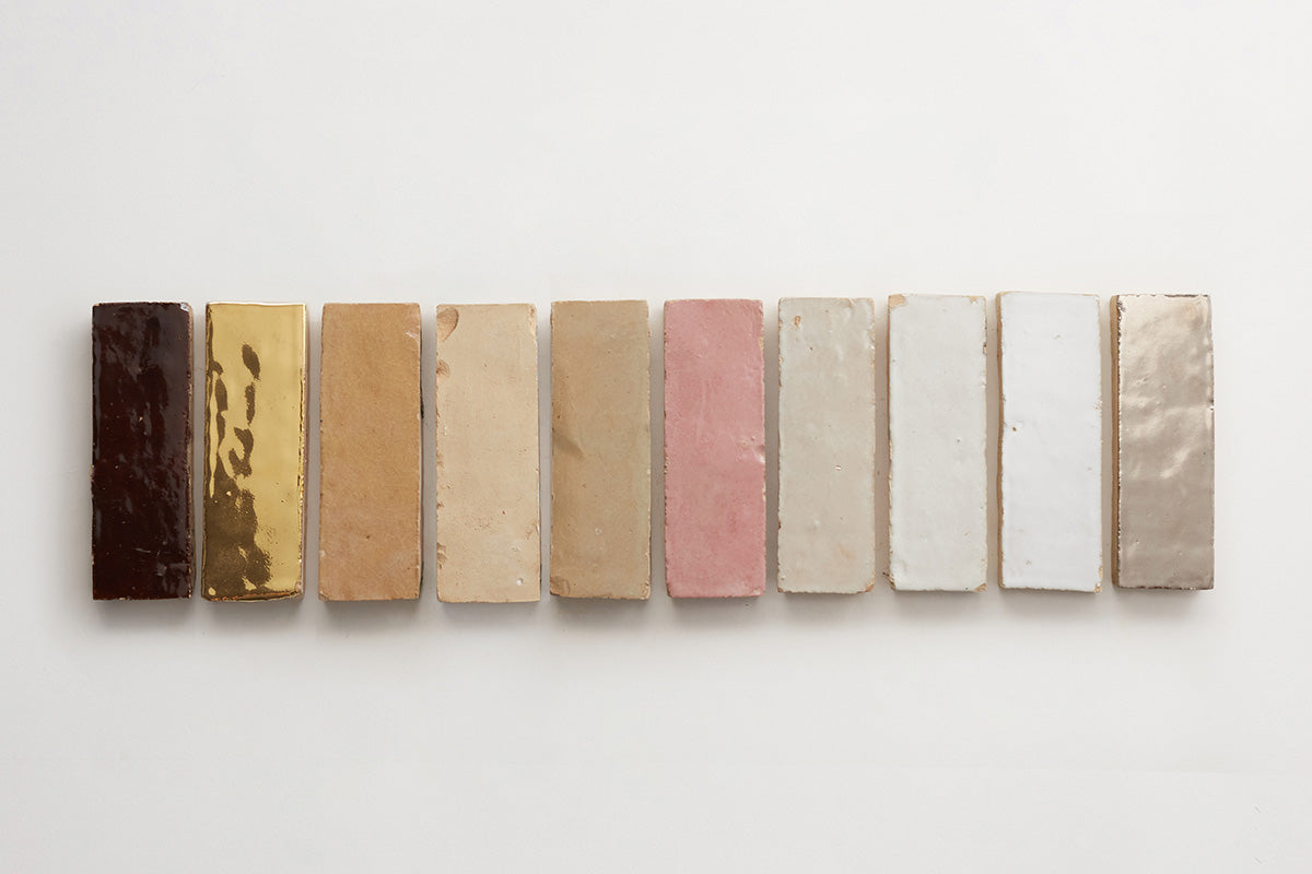 Tall rectangular zellige tiles laid out in a row from left to right, in neutral colors like tan, dark brown, gold, and pink.