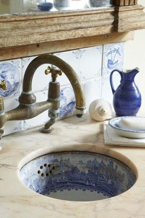 Delft tiles on the wall of a bathroom, as well as a blue and white cityscape in the sink bowl.