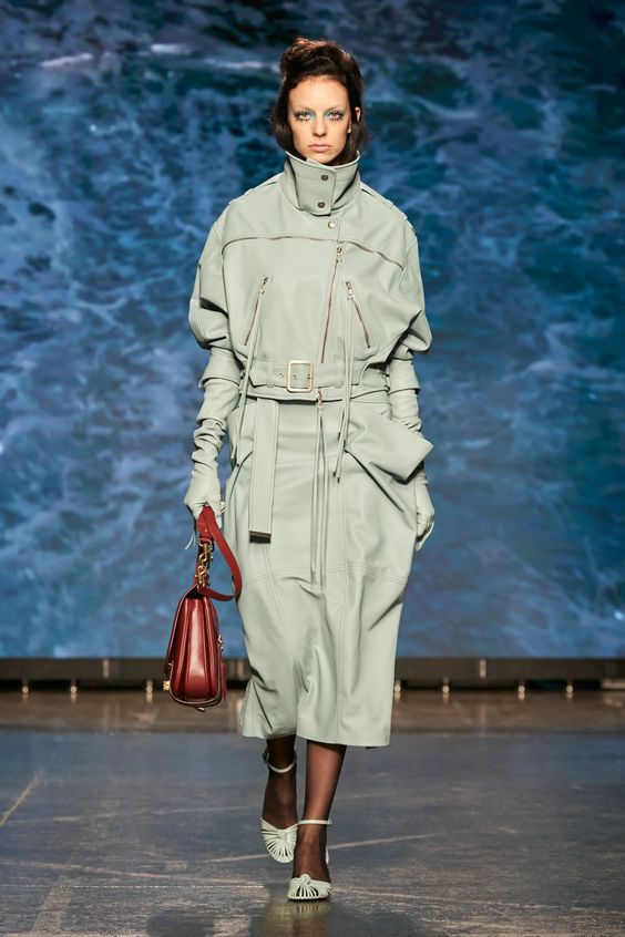 woman walking on runway wearing mint green dress and carrying a leather purse